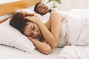 woman closing her ears after sleepless night with sleeping and snoring man in bed