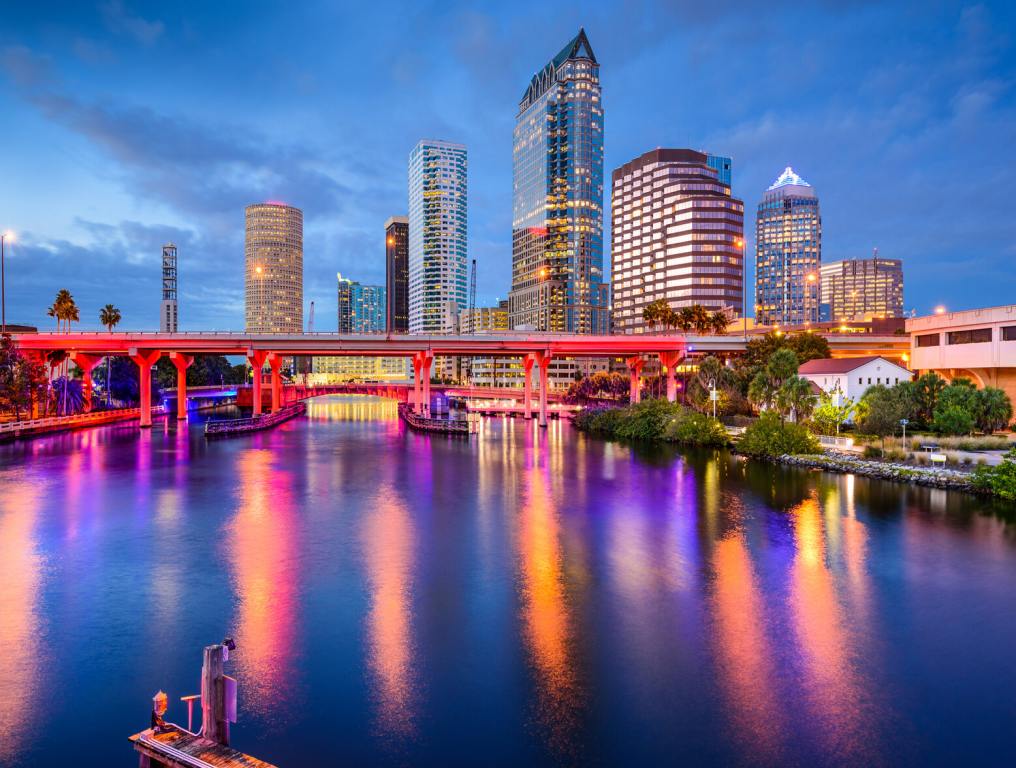 A colorful night photo over Tampa bay's river with the city skyline in the background reflecting off the calm water.