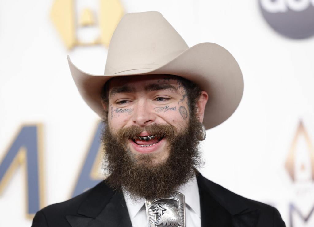 Post Malone attends the 57th Annual CMA Awards smiling wearing a cowboy hat.