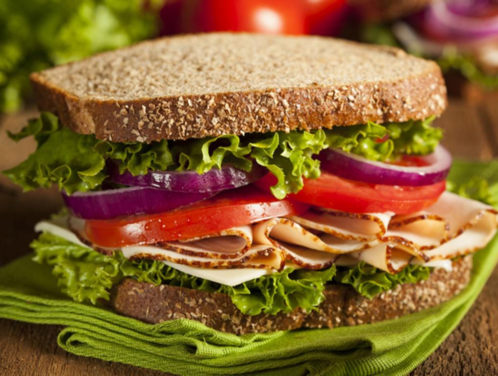 A sandwich with tomatoes, onions, and lettuce on wheat bread