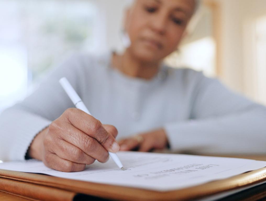 Senior woman, sign and writing with documents, paperwork and application for life insurance policy. Person, hand and checklist for compliance, investment or will in retirement with signature in home