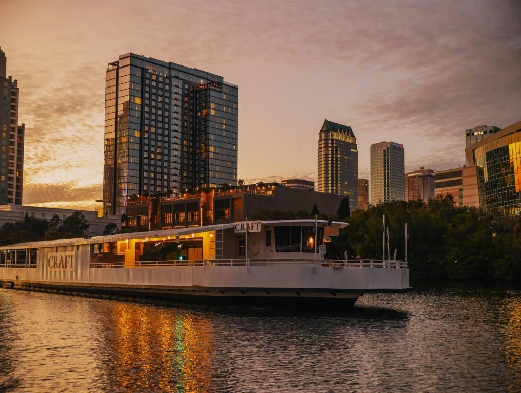 Craft Experiences Luxury Tampa Dinner Cruise boat sitting in the river with a Tampa Bay sunset skyline behind it.