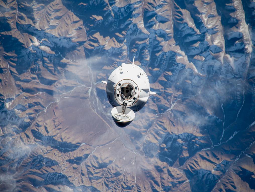 The SpaceX Dragon spacecraft above earth over mountains.