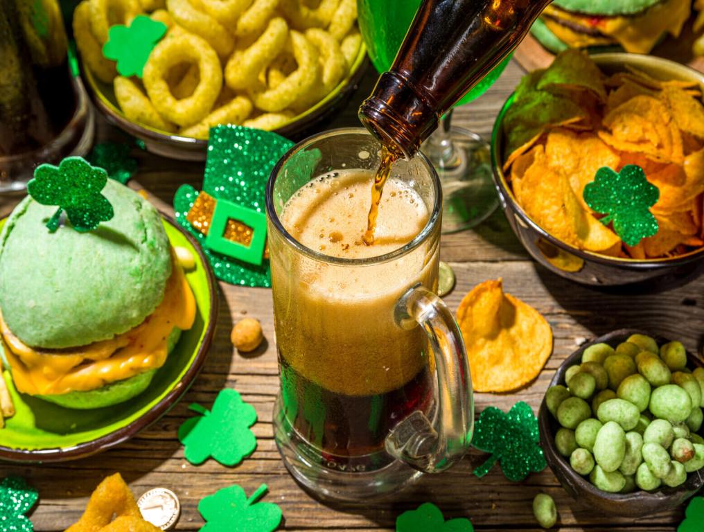 Assorted foods and Irish festivity pieces decorated on a wooden table in green.