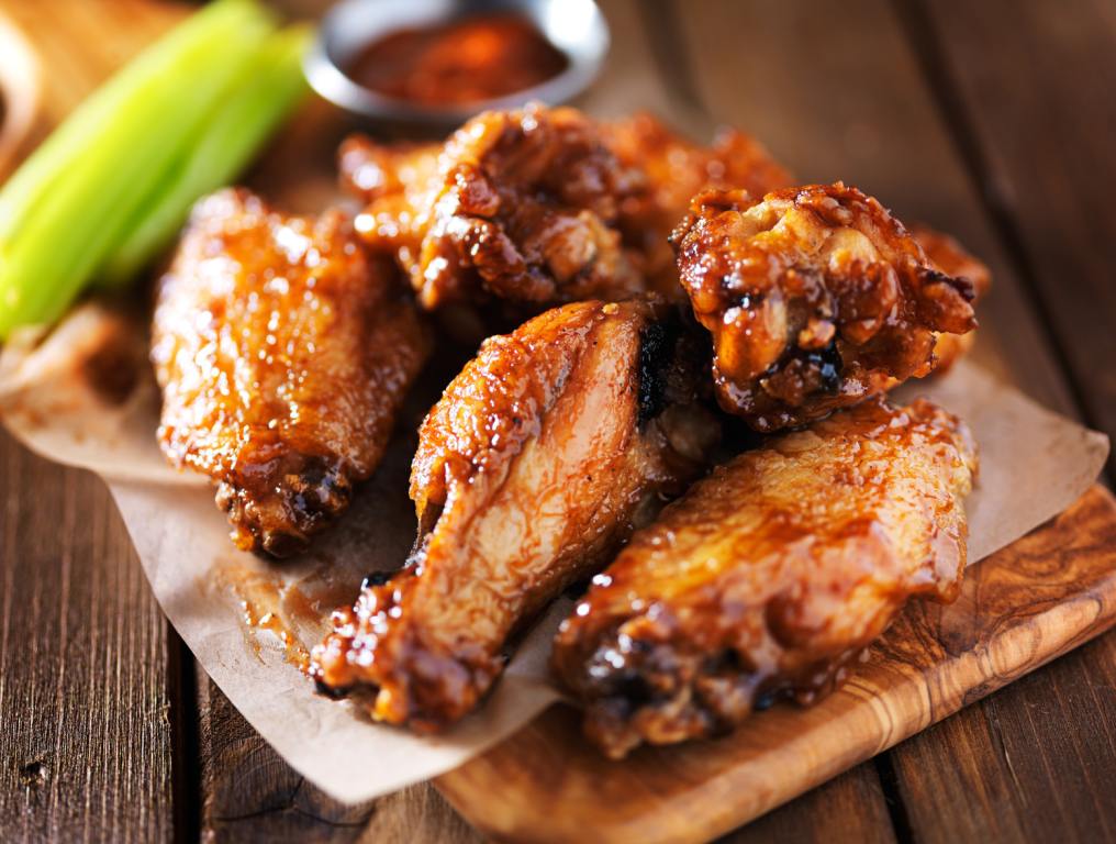 Juicy BBQ chicken wings on a wooden platter and celery on the side. NY-Style 'Sugar Wing' Expanding To Tampa Bay